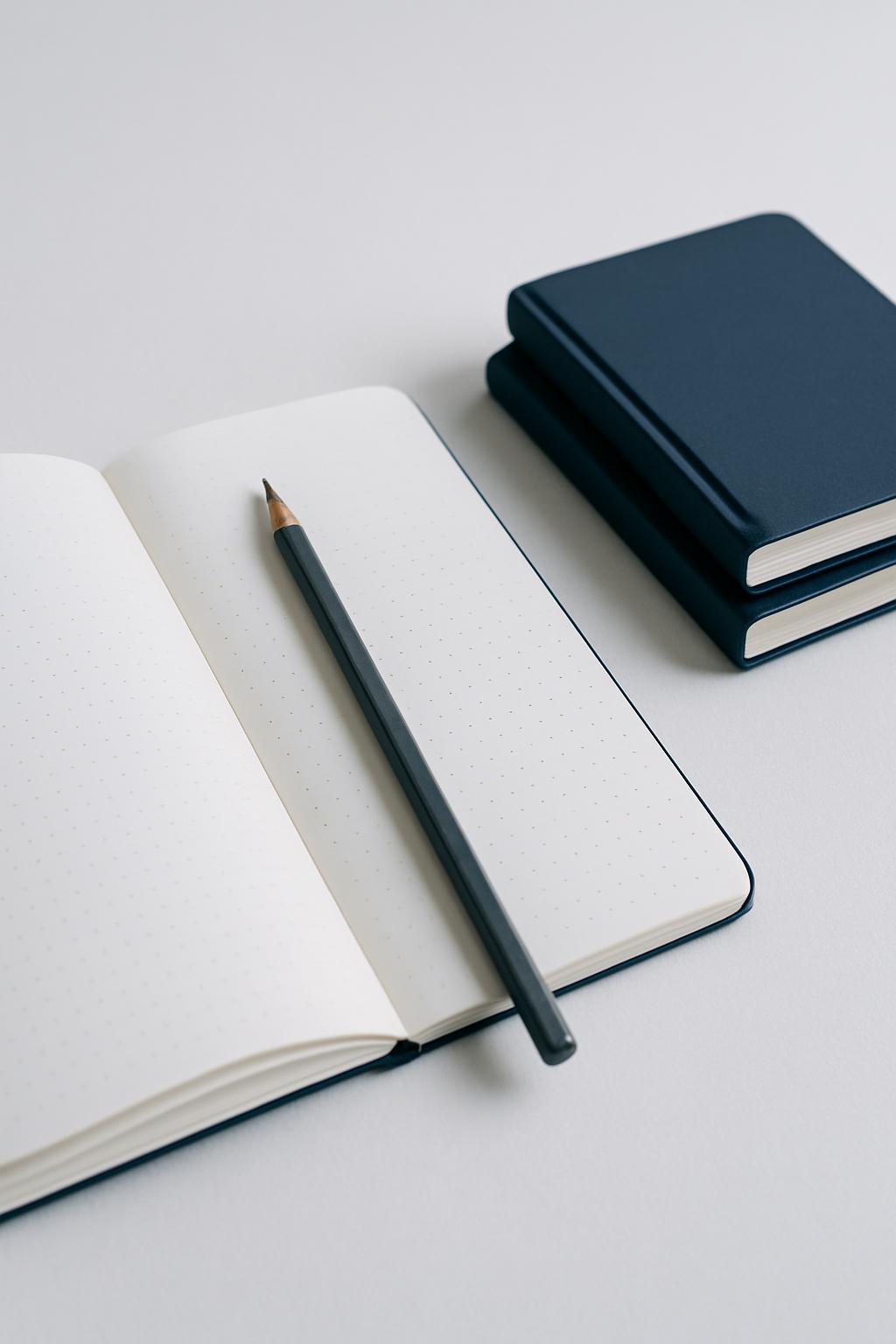 Open dotted notebook with a graphite pencil and two pocket books stacked beside it